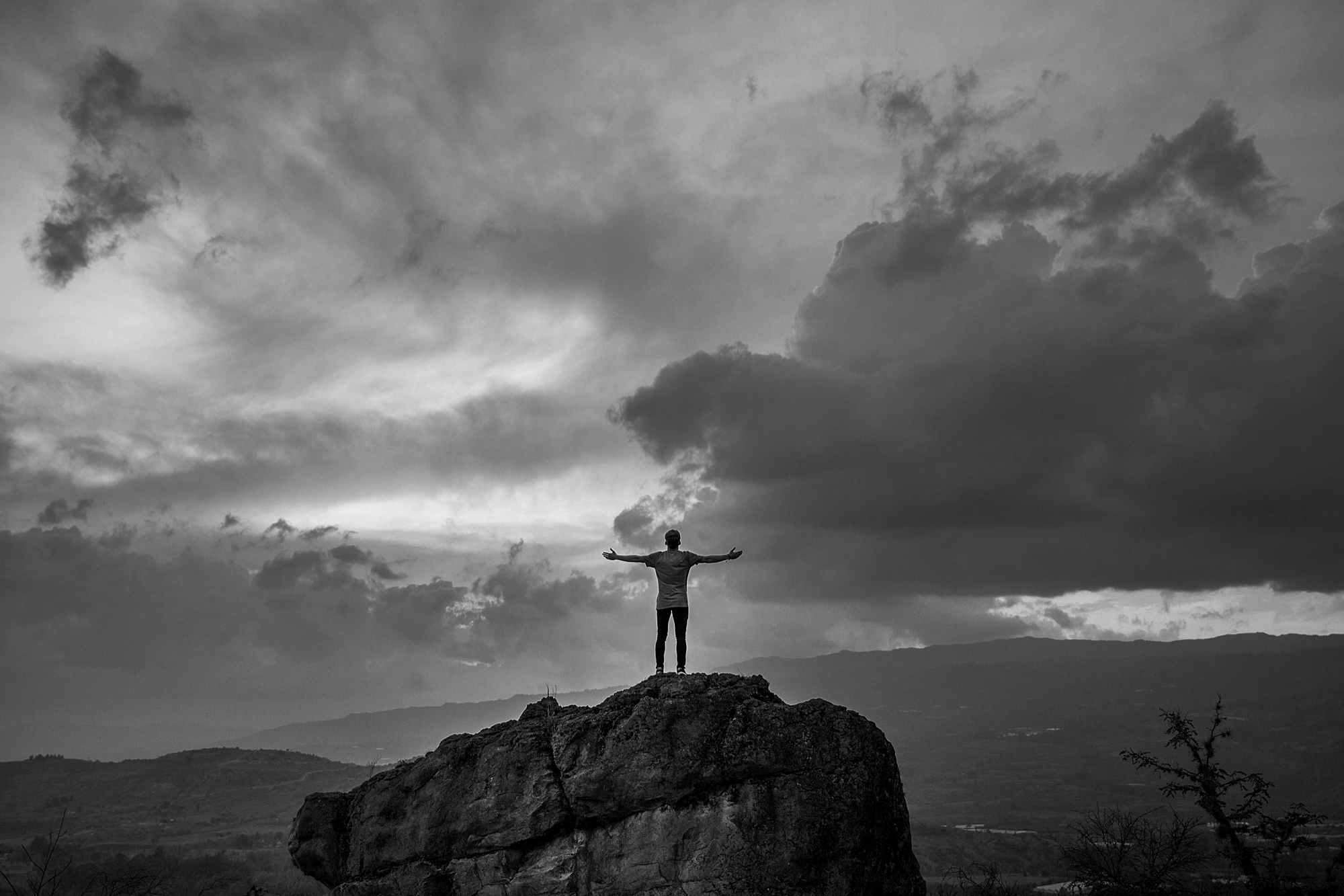 A figure standing on a rock outcrop, arms open, under a wide sky